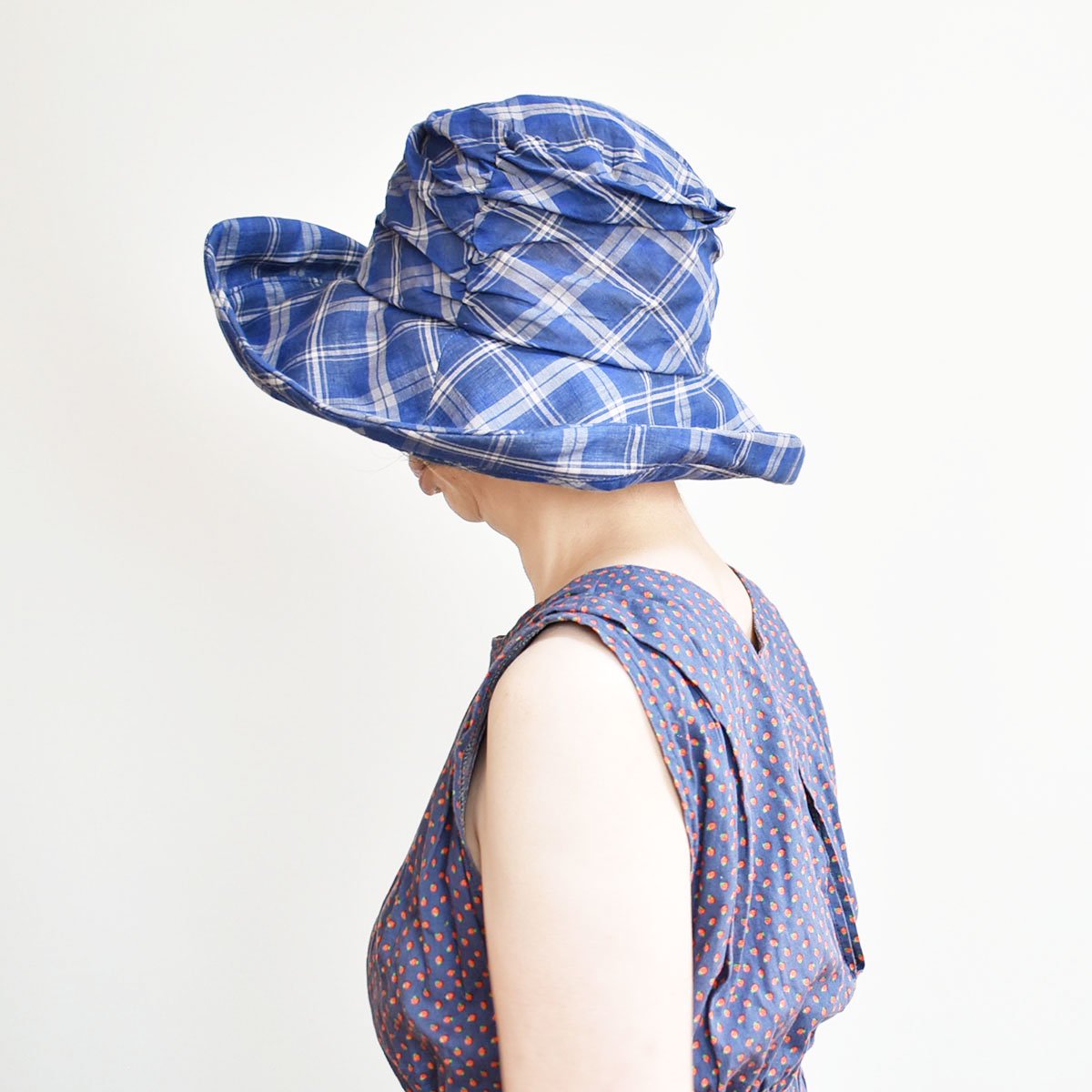 アシンメトリーヘムキャペリーヌ。爽やかなブルーのチェックのPeachBloomオリジナルデザインのキャペリーヌ（つば広帽子）。柔らかい素材のドレープ感とブリム（つば・ひさし）エッジの自在なアレンジで夏にピッタリの帽子。【PS0707】